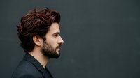 Male with reddish-brown wavy hair and full beard in profile against dark background, suitable for grooming, barbershop, and lifestyle marketing materials.