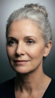Mature woman with gray hair styled in an updo, fair complexion, and neutral expression gazing toward camera against dark background for portrait and professional use.