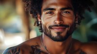 Handsome young mixed-race man with curly hair and beard smiling warmly at camera in natural outdoor setting with soft bokeh background lighting.