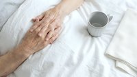 Elderly hands resting on white bedding with coffee cup, representing comfort, relaxation, morning routine, senior lifestyle, healthcare and peaceful moments.