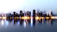 Modern cityscape with illuminated skyscrapers reflecting in calm water at dusk, creating mirror effect with blurred lights and soft focus for dreamy urban atmosphere.