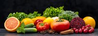 Fresh organic produce panorama with citrus, tomatoes, berries and herbs against dark background, healthy eating concept for food service and design.