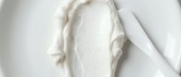 Creamy white cosmetic product spread on white surface with applicator, showcasing skincare texture for beauty and wellness marketing.