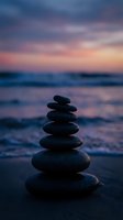 Zen stone stack on beach at sunset with colorful sky reflection in calm ocean waves creating peaceful meditation atmosphere for wellness and mindfulness concepts.
