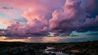 Dramatic storm clouds in vibrant pink and purple hues over rocky landscape at sunset creating moody atmospheric sky for nature photography backgrounds.