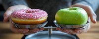 Pink frosted donut and fresh green apple balanced on scale plates showing contrast between healthy and unhealthy food choices for diet and nutrition concept.