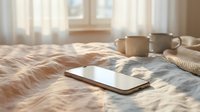 Cozy morning bedroom scene with laptop, coffee cups and warm sunlight streaming through window creating peaceful work from home atmosphere.