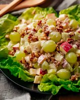 Fresh waldorf salad with green grapes, apples, celery, and walnuts served on crisp lettuce leaves, dressed in creamy mayonnaise dressing on dark plate.