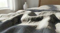 Cozy bedroom with rumpled striped bedding in neutral tones, soft morning light from window, and white ceramic vase on nightstand. Perfect for home decor, lifestyle, and interior design projects.