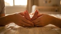Newborn baby feet cradled in parent hands during golden hour sunlight, symbolizing love, care, and family bonding in warm home setting.