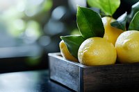 Fresh yellow lemons with green leaves in rustic wooden box on dark surface against blurred background, selective focus with copy space for food design.