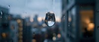 Raindrop on glass window with blurred city lights and urban skyline in background creating atmospheric bokeh effect during evening storm.