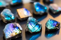 Vibrant labradorite gemstones displaying iridescent blue and purple flash effects on dark background, macro photography showing detailed crystal structure and play of light.