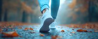Person in white sneakers walking on autumn path with fallen orange leaves. Close-up of feet in motion during outdoor exercise or jogging in fall season.