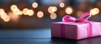 Pink gift box with bow against blurred golden bokeh lights background on dark surface, festive holiday celebration concept for special occasions.
