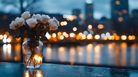 White roses in glass vase against evening cityscape with blurred bokeh lights reflecting on water surface, creating romantic mood for special occasions.