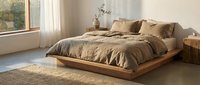Wooden platform bed with tan bedding in minimalist bedroom with natural light, wooden nightstand, and neutral decor for interior design projects.