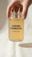 Hand holding glass jar of golden fermented tea drink with ginger and lemon flavor for healthy lifestyle and wellness nutrition.