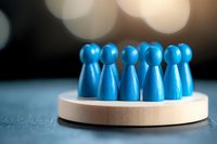 Blue wooden figures standing in circle on round platform against blurred background, representing teamwork, unity and collaboration in business concept.