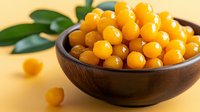 Fresh yellow gooseberries in wooden bowl on yellow background with green leaves, bright natural organic berries for healthy eating and desserts.