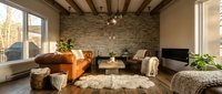 Spacious modern living room with exposed wooden beams, orange leather sofa, stone accent wall, large windows, neutral furnishings and natural light for interior design projects.