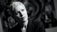 Mature woman with short white hair wearing black blazer, looking thoughtfully at camera in monochrome studio portrait for corporate, business, and professional headshot use.
