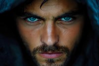 Intense close-up portrait featuring striking blue eyes and dark facial features against dramatic shadows, creating mysterious and powerful emotional impact.