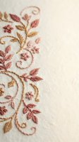 Delicate floral embroidery with pink and gold threads on cream fabric showcasing intricate needlework and decorative stitching for textile and craft projects.