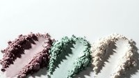 Colorful cosmetic powder swatches in purple, green and white creating artistic makeup strokes on clean background for beauty and fashion projects.