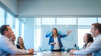 Professional businesswoman presenting to diverse team in modern conference room with large windows and city view during corporate meeting.
