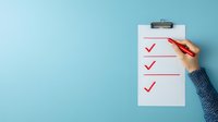 Female hand in blue sweater marking completed tasks with red checkmarks on white clipboard against turquoise background, representing productivity and goal achievement.