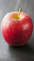 Fresh red apple with water droplets on smooth skin against dark background, macro photography highlighting natural texture and dewdrops for food marketing.