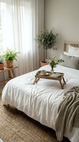 Cozy bedroom interior with breakfast tray on bed, natural light through white curtains, houseplants and minimalist decor for peaceful morning routine.