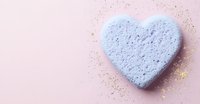Blue heart shaped bath bomb with golden glitter scattered on pink background. Spa and wellness concept for romantic self-care routines and Valentine's day promotions.