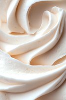 Creamy white whipped texture with soft swirls and curves creating an abstract pattern, macro photography showing smooth peaks and valleys in dairy dessert topping.