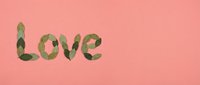 Word love spelled with green tropical leaves on soft pink background for romantic greeting cards and wedding invitations.