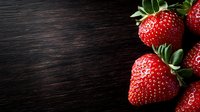 Fresh ripe strawberries with green leaves on dark wooden background with copy space. Natural lighting creates dramatic mood for food photography.