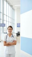 Confident female doctor with stethoscope standing in modern hospital corridor with arms crossed, smiling at camera in bright medical facility.