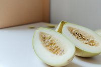 Fresh honeydew melon cut in half showing juicy flesh and seeds on white surface, minimalist food photography with soft natural lighting and shallow depth of field.