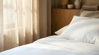 Comfortable bed with white linens and pillows in a bright bedroom with sheer curtains and wooden furniture for hospitality and home decor.
