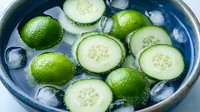 Sliced cucumber and fresh limes floating in ice water inside blue bowl, perfect for refreshing beverages, spa treatments, and wellness content.