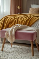 Cozy bedroom corner with pink velvet ottoman, draped cream throw blanket, mustard yellow bedding, and plush white carpet creating warm minimalist interior design.