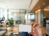 Mature male professional holding blank white business card in modern office lobby with glass partitions and contemporary interior design.