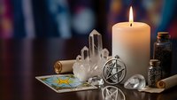 Mystical altar setup with burning candle, crystal cluster, pentagram pendant, tarot cards and glass bottles for spiritual practices and divination.