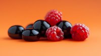 Fresh ripe raspberries and black cherries on vibrant orange background, macro food photography showing juicy summer berries with natural lighting.