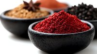 Colorful spices in dark bowls including red sumac, black peppercorns and ground cinnamon with star anise for cooking and seasoning recipes.