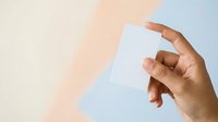 A person with medium skin tone holds a blank white card against a soft pastel background, suitable for business cards, invitations, or promotional materials.