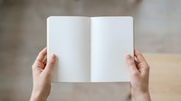 Hands holding open blank notebook with white pages for mockup, branding, or publishing design projects.