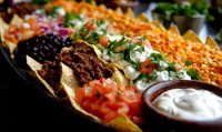 Mexican food platter with crispy tacos filled with seasoned meat, fresh pico de gallo, black beans, shredded cheese, sour cream and colorful toppings served on dark plate.