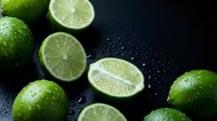 Fresh green limes with water droplets on dark background. Citrus fruits cut in half showing juicy pulp. Healthy organic produce for cooking and beverages.